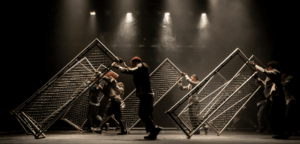 Bailarinos do Grupo Corpo Molde em cena no espetáculo '3ª', com cenografia de grades metálicas simbolizando a tensão e transformação do corpo humano e da sociedade.