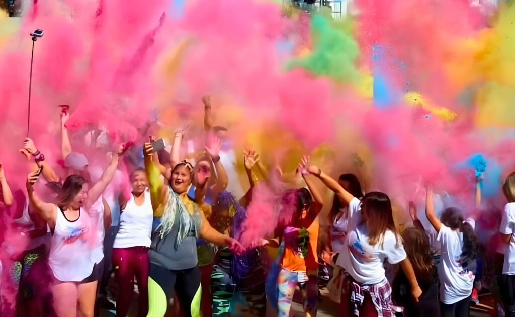 Participantes do Agita Comunidade Collors 2026 dançando e se divertindo no Parque da Juventude, com explosão de cores ao fundo.